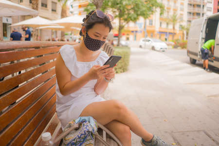 city lifestyle portrait of young beautiful and relaxed Asian woman in face mask against covid19...