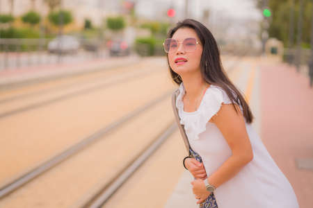 young beautiful Asian woman waiting for train - lifestyle portrait of attractive and happy Korean girl at railway platform waiting relaxed in transport conceptの写真素材