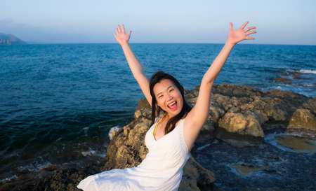 young Asian woman by blue sea -  happy and beautiful Chinese girl  enjoying holiday trip playful and cheerful at beach rock cliff during summer in tourist  travel conceptの写真素材