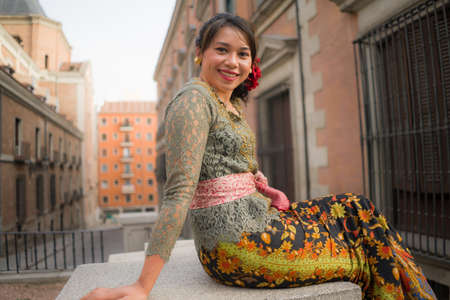 young happy and beautiful Asian woman wearing traditional Balinese kebaya dress - Indonesian girl in Bali clothes walking on street during holidays travel in Europeの写真素材