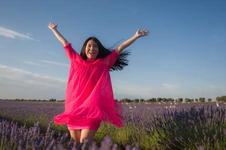 young Asian woman outdoors at lavender flowers field - happy and beautiful Chinese girl in sweet Summer magenta dress enjoying holidays relaxed on purple floral meadowの写真素材