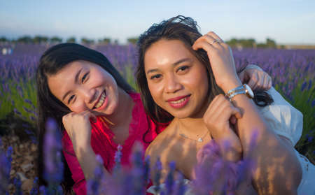 young happy and beautiful Asian korean woman playing on lavender flowers field with her hispanic girlfriend enjoying sweet holidays together relaxed and carefreeの写真素材