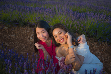 young happy and beautiful Asian korean woman playing on lavender flowers field with her hispanic girlfriend enjoying sweet holidays together relaxed and carefreeの写真素材