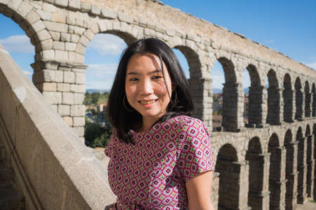Attractive Asian girl during vacation in Spain - young happy and beautiful Chinese woman visiting heritage aqueduct in Segovia enjoying holidays travelの写真素材