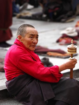 Lhasa, Tibet, China - 07/24/2010: Tibetan pilgrim woman sitting on stair spinning a prayer wheelのeditorial素材