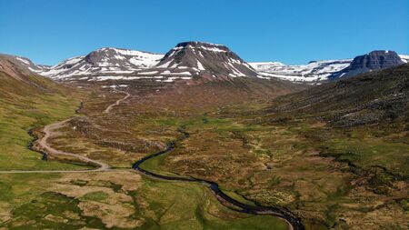 Scenic aerial view of typical Icelandic landscape with rivers meandering through green fields and snowcapped mountains in the background, summer scene with a bright blue sky, Bolungarvik, Westfjords, Iceland. Panorama shot by drone camera.の写真素材