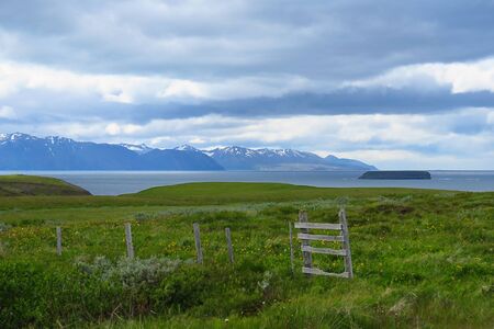 Fence in field, green grass, fjord lake and mountains in the background, Tjornes peninsula, Iceland, Europeの写真素材