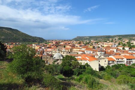 Panoramic view over the old town of Bosa, the church and typical houses with red roofs surrounded by mountains and the Mediterranean Sea in the distance, Sardinia, Italy, Europeの写真素材