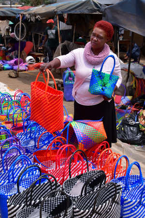 Manzini, Swaziland - 10/30/2019: African woman selling colorful woven shopping bags at the local market, Eswatini, Africaのeditorial素材