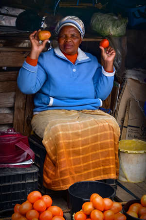 Manzini, Swaziland - October 30, 2019: African woman selling and promoting fresh tomatoes at the local marketのeditorial素材