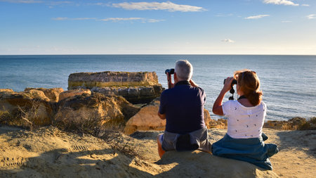 Costa da Caparica, Algarve - November 3, 2021: Couple with binoculars watching sea birds on the...