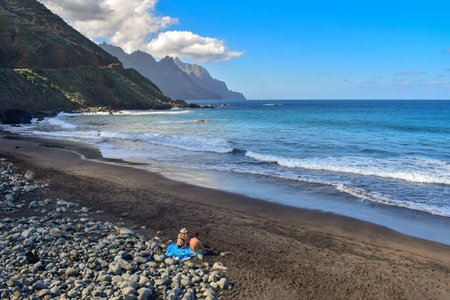 Couple on black sand beach enjoying the scenic north coast of Tenerife, wild Canary Islands landscape, beauty of Spain, travel Europeの写真素材