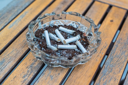 Ashtray with lit cigarette on a wooden tableの写真素材