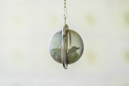Suspended metal tea infuser with dried leaves of green tea and mint on clean background