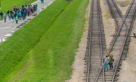 Oswiencim, Poland - September 21, 2019: Groups of Tourists walk along the train line where the wagons arrived with the Birkenau prisoners.のeditorial素材