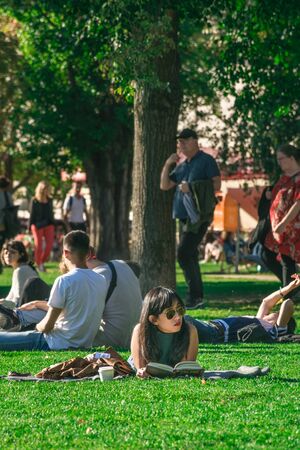 BERLIN, GERMANY - SEPTEMBER 26, 2018: Vertical view of a woman with sunglasses laying in grass reading at the James Simon Park, next to the Museum Island and behind the Cathedral of Berlinのeditorial素材