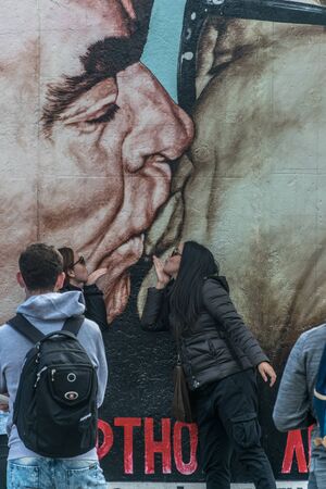 BERLIN, GERMANY - September 26, 2018: Tourists taking pictures near the The Kiss painting at the Berlin Wall, an iconic image of the Soviet leader and the East Germany President kissing with passionのeditorial素材