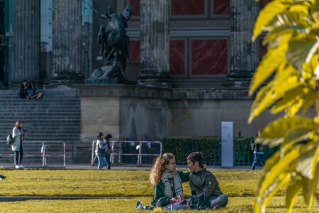 BERLIN, GERMANY - July 28, 2018: Passionate couple sitting in the grass and enjoying the sunlight at the Lustgarten a park of the Museum Island, in front of the Altes Museum, a world heritage buildingのeditorial素材