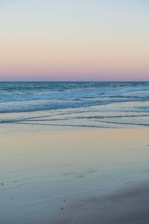 Slow motion of the ocean waves in a calm afternoon near the sunset time with a pink and pastel color palette in the empty beach of Trancoso at Bahia, Porto Seguro, a common tourism areaの写真素材