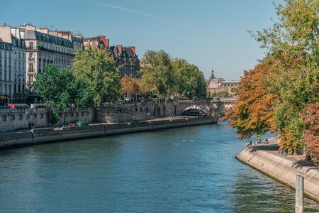Perspective of the natural Seine river among the urban environment of Paris, France, with voluptuous trees and people relaxing at the margins near classical buildings during the dayの写真素材