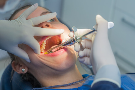 Great concept of dental procedure, young blond Brazilian woman in dental chair suffering dental procedure by dentist.の写真素材