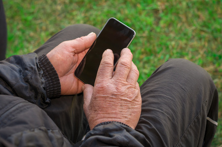 Close up of a wrinkled finger touching the smartphone, old man uses technology. Internet.の写真素材
