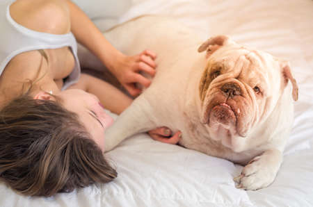 Beautiful woman sleeping in bed with english bulldog puppy.の写真素材