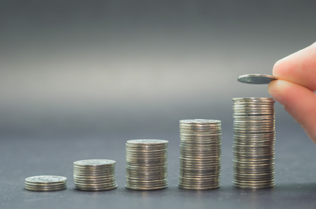 Great concept of savings, economy. Hand adding coin into pile of coins.の写真素材