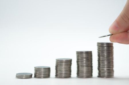 Great concept of savings, economy. Hand adding coin into pile of coins.の写真素材