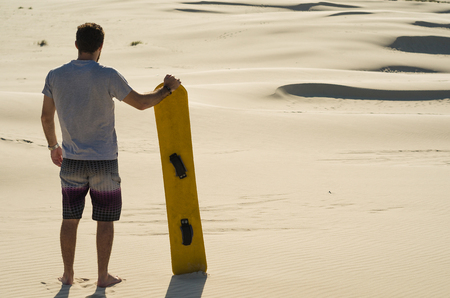 Young man on his back looking at the sand dunes, preparing to practice sandboarding.の写真素材