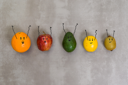 Great concept of healthy eating, diverse fruits with happy faces and arms upwards in gray background, polished concrete. Orange, apple, kiwi, lemon.の写真素材