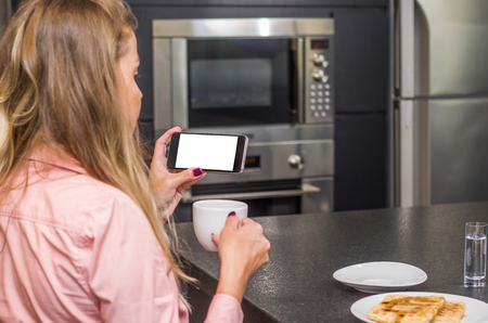 Young woman using smartphone drinking coffee, breakfast.の写真素材