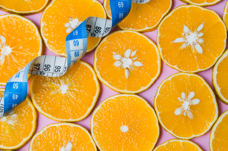 Background for healthy eating concept, beautiful texture of orange slices on pink background with measuring tapeの写真素材