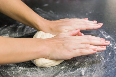 Woman preparing pizza dough on black granite table