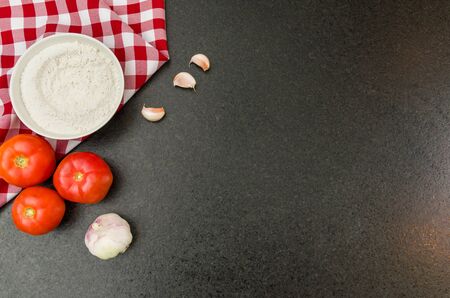 Great background for gastronomic theme like pizza, with space for information, background with tomatoes, wheat flour, garlic, basil leaves on black granite background. Copy Space.の写真素材
