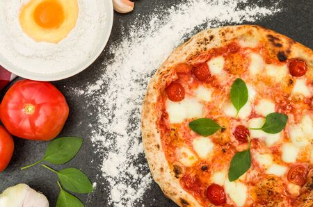 Great background for culinary themes, handmade pizza with marguerite flavor on black granite background with different ingredients.の写真素材