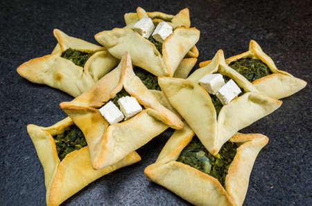 Delicious Lebanese (Arabic) food, spinach sfiha with ricotta cheese on black stone background.