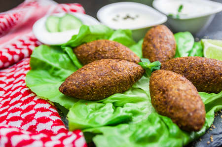 Delicious Lebanese (Arabic) food, kibbeh (kibe) with sauces and lemon on black slate stone and granite background with traditional keffyeh.の写真素材