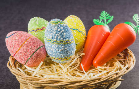 Easter colored eggs and carrots in a basket isolated on a trendy black background. Minimal easter concept. Easter card with copy space for text.の写真素材