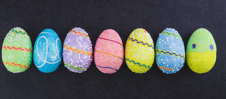 Colorful Easter eggs lined up side by side on a trendy black background.の写真素材