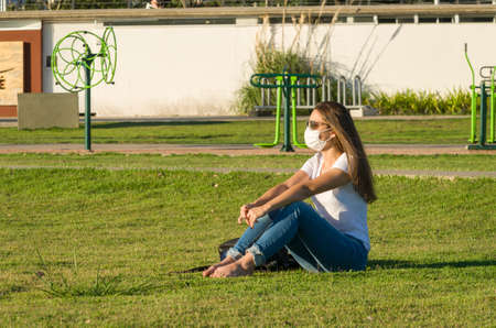 Young woman sitting on the grass with a protective mask during the SARS CoV-2 pandemic season , on the new Orla do Guaiba in Porto Alegreの写真素材