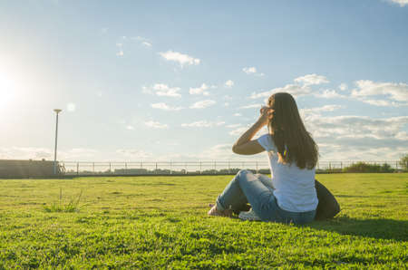 Young woman sitting on the grass with a protective mask during the SARS CoV-2 pandemic season , on...