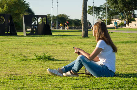 Young woman sitting on the grass with a protective mask during the SARS CoV-2 pandemic season , on the new Orla do Guaiba in Porto Alegreの写真素材