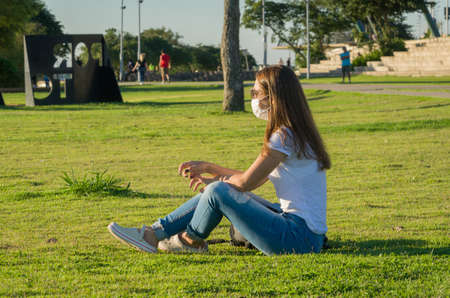 Young woman sitting on the grass with a protective mask during the SARS CoV-2 pandemic season , on the new Orla do Guaiba in Porto Alegreの写真素材