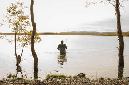 Sport fisherman fishing in lake on cloudy dayの写真素材