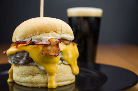 Close-up of tasty homemade bacon burger and cheddar sauce on wooden table and black backgroundの写真素材