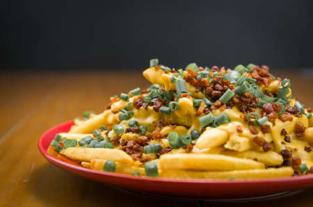 Tasty french fries, cheddar and bacon close-up on wooden and black backgroundの写真素材