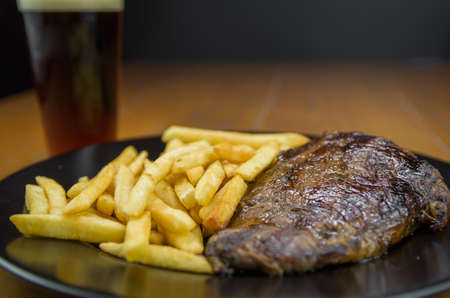 Delicious grilled entrecote dish with french fries and glass of beerの写真素材