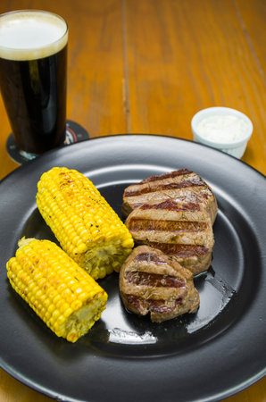 Delicious filet mignon close-up with roasted corn and glass of beer.の写真素材