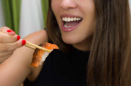 Woman eating delicious sushi, closeup on chopsticksの写真素材